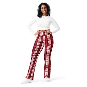 Op de afbeelding: Een vrouw draagt een witte crop top met lange mouwen en een legging met een rood, zwart en wit patroon. De legging heeft een herhalend geometrisch ontwerp. De vrouw lacht en heeft haar handen in haar zij. Ze draagt witte sneakers.