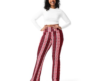 May include: A woman wearing a white long-sleeve crop top and red, black, and white patterned leggings. The leggings feature a repeating geometric design. The woman is standing with her hands on her hips, smiling at the camera. She is wearing white sneakers.
