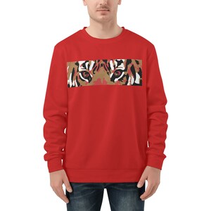 Op de afbeelding: Rode sweatshirt met een rechthoekige afbeelding van tijgerogen. De afbeelding gebruikt bruine, witte en zwarte tinten, met de ogen van de tijger in het midden. De sweatshirt heeft een effen rode kleur.