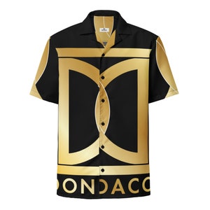 Op de afbeelding: Een zwart en gouden, kortgemouwd overhemd met knopen, met een geometrisch patroon en het woord "ONDACO" gedrukt op de onderkant.