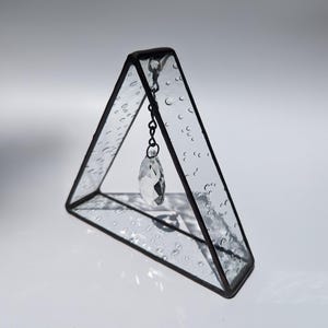 May include: A small glass triangle with a textured surface and a crystal hanging from a chain inside.