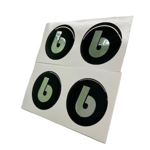 May include: Four black, circular stickers with a glossy finish. Each sticker features a light green letter "b" inside a black circle. The stickers are arranged in two rows of two on a white backing.