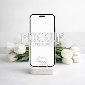 May include: A black smartphone mockup with a white screen, resting on a white stand. The word "MOCKUP" is displayed in a light gray font. White tulips are arranged behind the phone, with the text "P&D & JPG" below the word "MOCKUP".