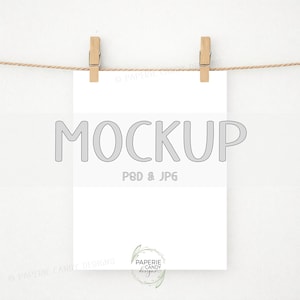 May include: A white paper mockup suspended by two wooden clothespins on a natural twine string. The word "MOCKUP" is printed in gray, along with "PSD & JPG". The bottom right corner features a logo with the text "PAPERIE CANDY designs".
