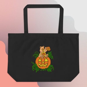 Puede incluir: Bolsa de tela negra con un gráfico de un oso de dibujos animados sentado en una calabaza. El oso sostiene una pequeña calabaza. El gráfico está rodeado de enredaderas verdes.