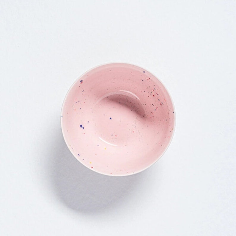 Peut inclure: Un bol en c&eacute;ramique rose avec un motif mouchet&eacute; dans des tons de bleu, jaune et rouge.