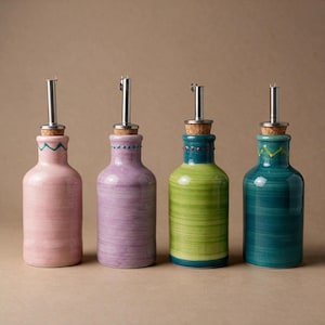 Könnte beinhalten: Vier Keramik-Ölspender in Rosa, Lavendel, Limettengrün und Blaugrün. Jede Flasche hat ein handgemaltes Muster am Hals, einen Korkstopfen und einen Ausgießer aus Edelstahl. Die Flaschen haben eine glatte, glänzende Oberfläche und runde Körper.
