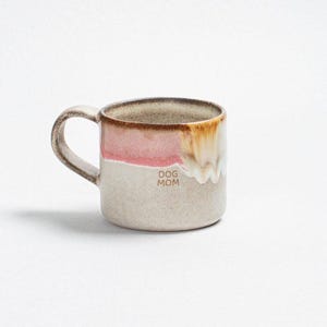 Könnte beinhalten: Eine Keramik-Tasse mit Henkel, mit einem farbblockierten Design in Rosa-, Beige- und Brauntönen. Auf der Tasse steht der Text "DOG MOM". Die Tasse ist für Heißgetränke konzipiert.