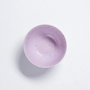 Peut inclure: Un bol en c&eacute;ramique de couleur lilas clair avec un motif mouchet&eacute; dans des tons d'orange, de bleu et de blanc.