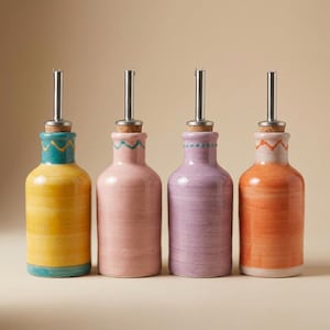 Könnte beinhalten: Vier farbenfrohe Keramik-Ölflaschen mit Edelstahl-Ausgießern. Die Flaschen sind in Gelb, Rosa, Lila und Orange bemalt, jede mit einem dekorativen Band am oberen Rand. Korken vervollständigen das Design. Ein stilvolles Küchenaccessoire.