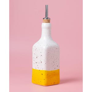 Könnte beinhalten: Weiße Keramikflasche mit gelbem Boden und einem Ausgießer aus Edelstahl. Die Flasche hat eine gesprenkelte weiße Glasur.