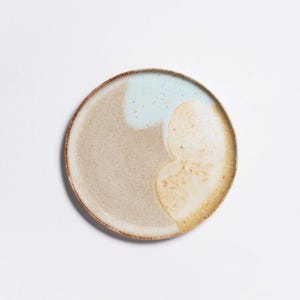 Könnte beinhalten: Ein runder Keramikteller mit hellbrauner, beiger und blauer Glasur. Die Glasur hat ein geflecktes, abstraktes Design.