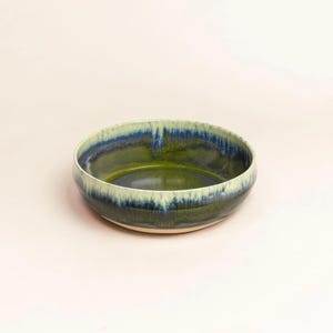 Könnte beinhalten: Eine runde Keramikschale mit grünem Innenraum und einem Rand, der von Blau zu Hellgrün verläuft. Die Schale hat ein schlichtes, modernes Design und eignet sich zum Servieren von Speisen oder als dekoratives Element.