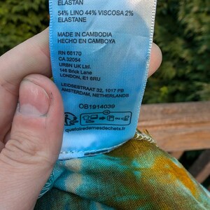 Peut inclure: Une &eacute;tiquette d'entretien en tissu bleu avec du texte blanc. L'&eacute;tiquette indique la composition du tissu comme &eacute;tant 54% lin, 44% viscose et 2% &eacute;lasthanne. Elle comprend &eacute;galement le pays d'origine, "Fabriqu&eacute; au Cambodge", et les coordonn&eacute;es de l'entreprise.