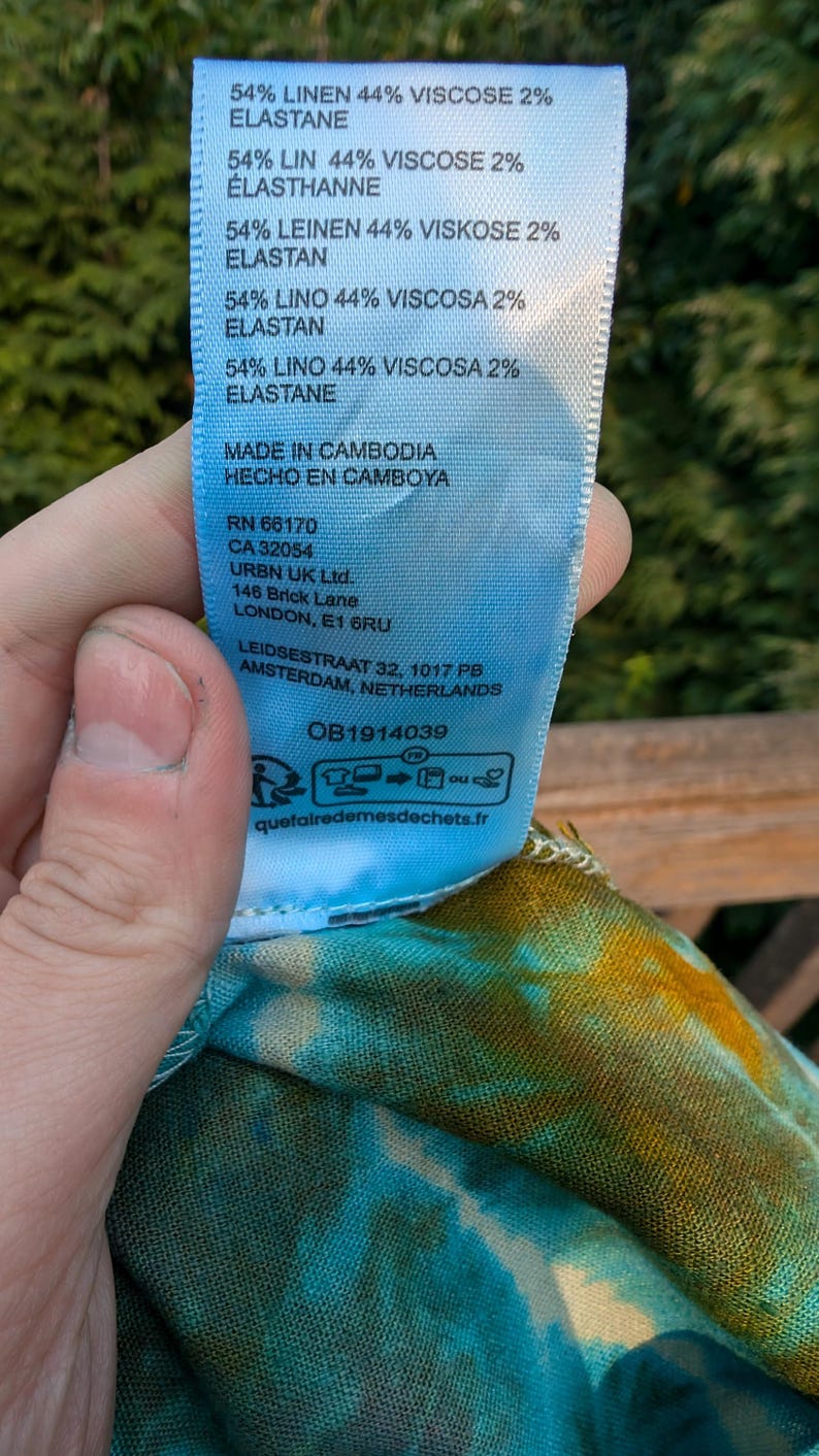 Peut inclure: Une &eacute;tiquette d'entretien en tissu bleu avec du texte blanc. L'&eacute;tiquette indique la composition du tissu comme &eacute;tant 54% lin, 44% viscose et 2% &eacute;lasthanne. Elle comprend &eacute;galement le pays d'origine, "Fabriqu&eacute; au Cambodge", et les coordonn&eacute;es de l'entreprise.