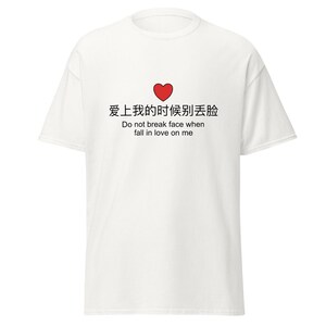 以下が含まれることがあります： 赤いハートのグラフィックと、英語のテキスト「Do not break face when fall in love on me」の上に中国語の文字がプリントされた白いTシャツ。