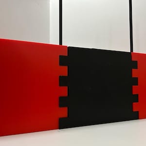 May include: A modular, geometric art piece composed of three connected panels. The outer panels are a vibrant red, while the central panel is black. The edges of the panels interlock, creating a visually interesting design.