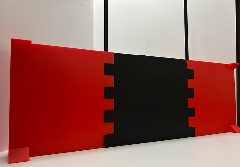 May include: A modular, geometric art piece composed of three connected panels. The outer panels are a vibrant red, while the central panel is black. The edges of the panels interlock, creating a visually interesting design.