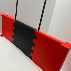 May include: A red and black rectangular object with two black vertical rods. The object has a notched design where the red and black sections meet. The object has small rectangular feet.