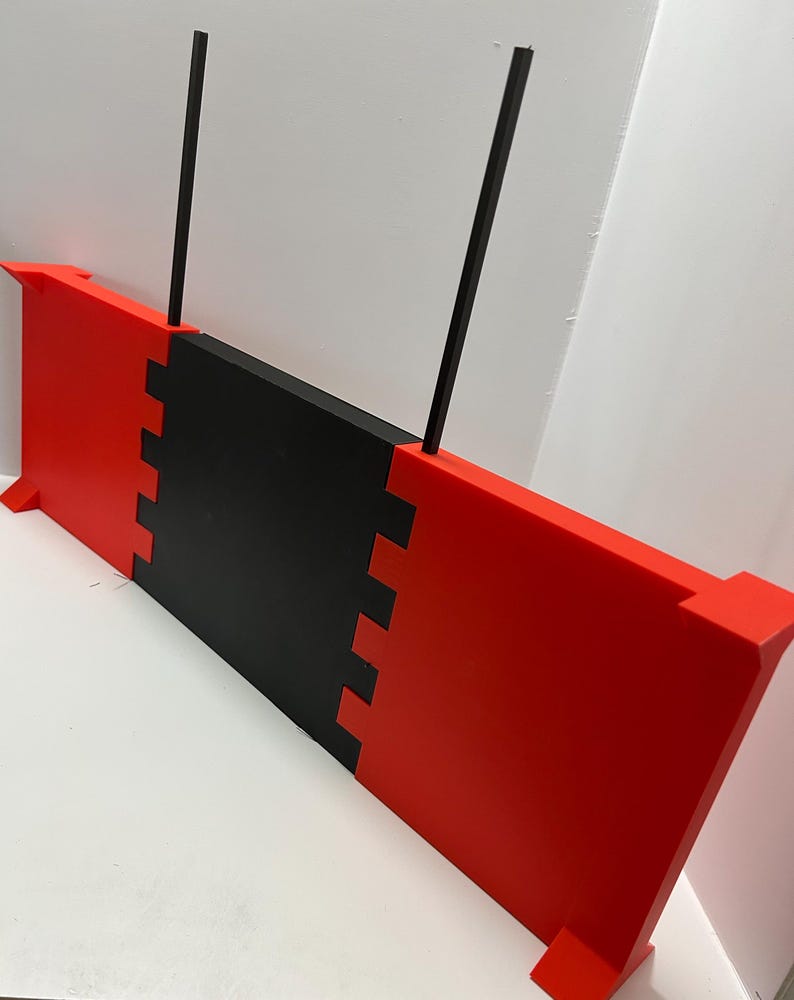 May include: A red and black rectangular object with two black vertical rods. The object has a notched design where the red and black sections meet. The object has small rectangular feet.