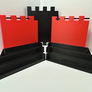 May include: A set of black and red castle-themed building blocks. The set includes red wall pieces with black horizontal bars and black base pieces. The blocks are arranged on a white surface.
