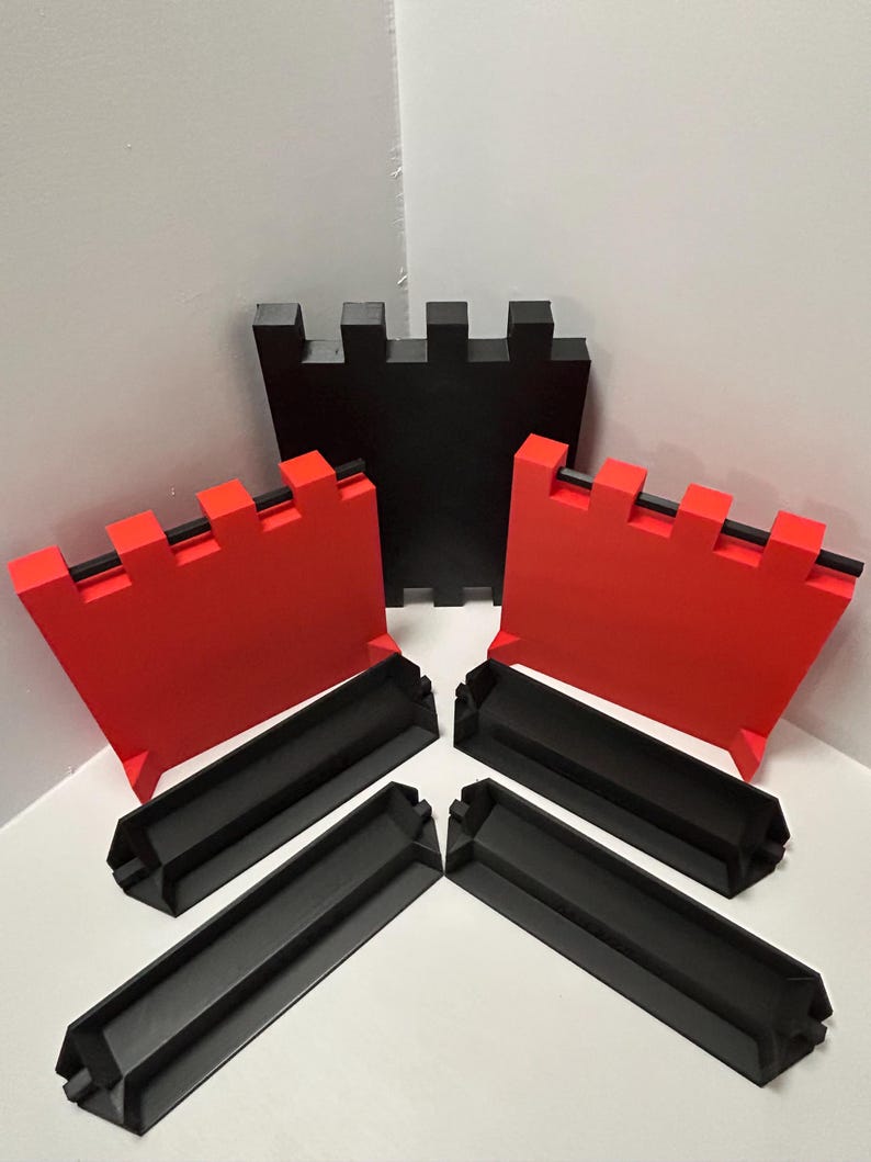 May include: A set of black and red castle-themed building blocks. The set includes three red crenelated wall pieces, one black crenelated wall piece, and four black base pieces. The blocks are arranged on a white surface.