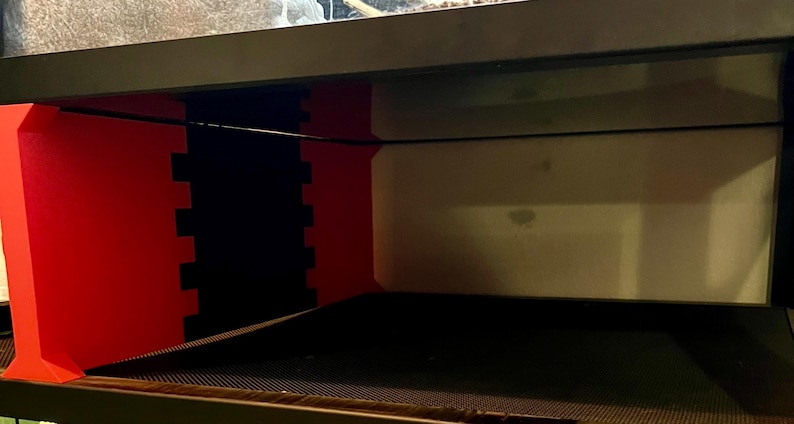 May include: A black and red terrarium with a black wire and a mesh bottom. The terrarium has a red support structure with a black, interlocking design. The background is a light beige color.