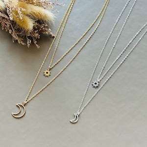 May include: Two layered necklaces with a crescent moon pendant and a sun pendant. One necklace is gold and the other is silver.