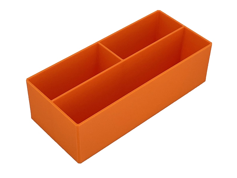 May include: An orange desk tidy with three compartments. The organiser is rectangular and made from a solid material. It is designed to hold pens, pencils, or other stationery items. The compartments are different sizes.