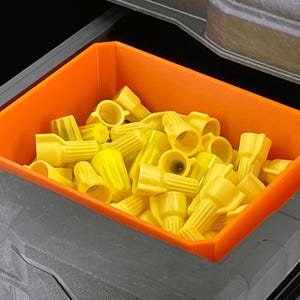 May include: An orange plastic bin filled with yellow wire connectors. The bin is rectangular and sits inside a larger gray container. The connectors are cone-shaped and have a ribbed texture.