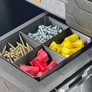 Pu&ograve; includere: Un organizer per cassetti con quattro scomparti riempiti con vari articoli hardware. Gli scomparti contengono viti dorate, bulloni argentati, connettori per cavi rossi e gialli. L'organizer &egrave; nero e si trova all'interno di un contenitore grigio pi&ugrave; grande.