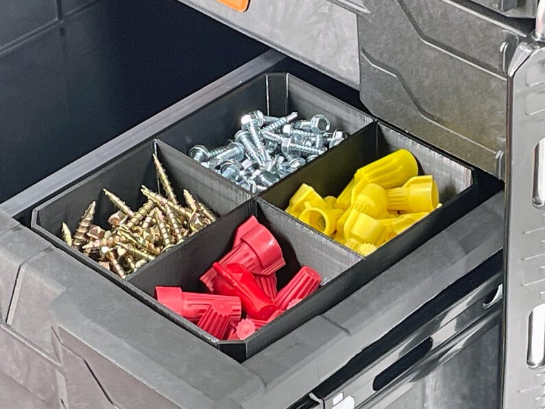 Pu&ograve; includere: Un organizer per cassetti con quattro scomparti riempiti con vari articoli hardware. Gli scomparti contengono viti dorate, bulloni argentati, connettori per cavi rossi e gialli. L'organizer &egrave; nero e si trova all'interno di un contenitore grigio pi&ugrave; grande.