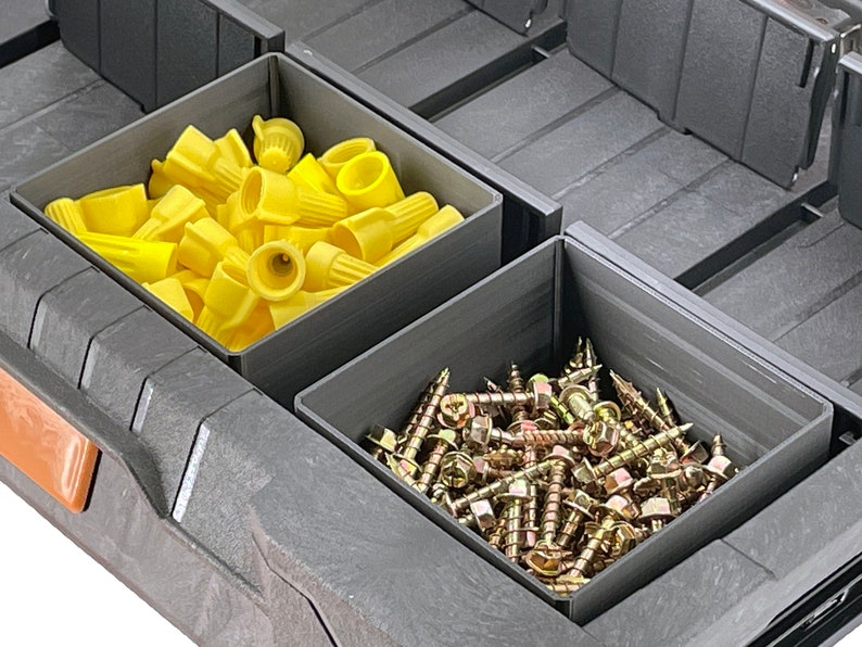 May include: A gray plastic storage box with two compartments. The top compartment is filled with yellow wire connectors. The bottom compartment is filled with gold screws.