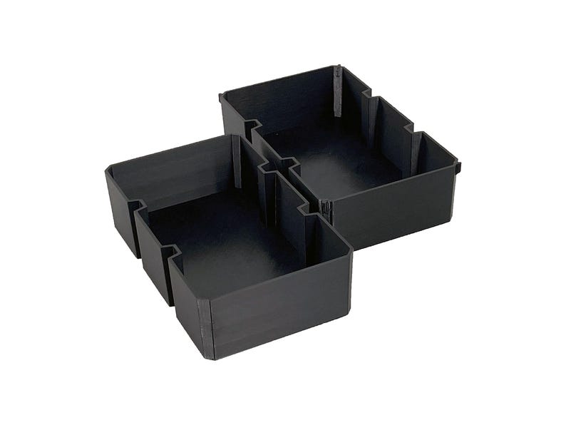 May include: Black plastic storage organizers in various sizes, designed to interlock. The organizers have a simple, rectangular shape with open tops and are suitable for organizing items in drawers or on shelves.