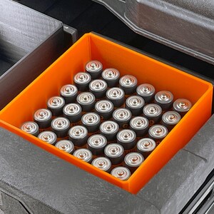 May include: An orange plastic storage container filled with a large quantity of AA batteries.