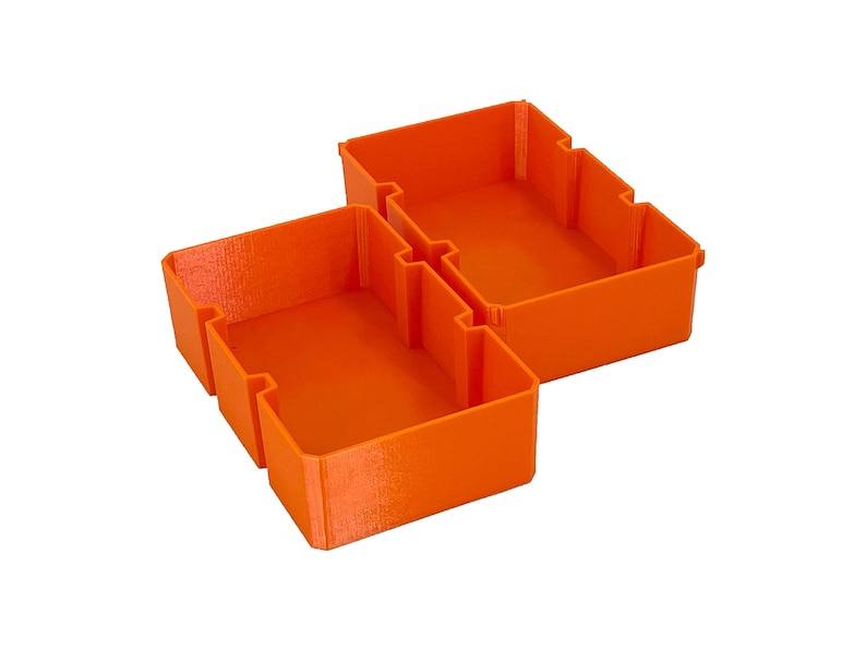 May include: Three bright orange storage bins, designed to interlock. The bins are rectangular with notched sides, and are made of a textured plastic material. The bins are empty and set against a white background.