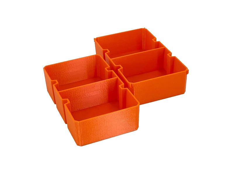 May include: Four orange plastic storage bins, each with a rectangular shape and open top. The bins are interlocked, creating a modular storage system. The bins are made of a textured plastic.