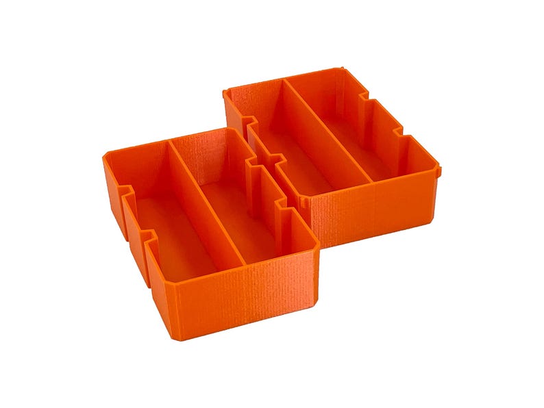 May include: Two bright orange, rectangular storage containers with internal dividers. The containers are made of a solid material and are designed to organize small items. The containers are shown against a white background.