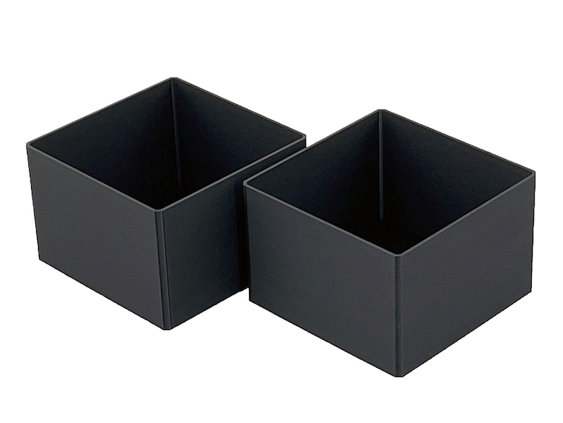 May include: Two black square-shaped storage boxes made of plastic. The boxes are empty and are sitting next to each other on a white background.