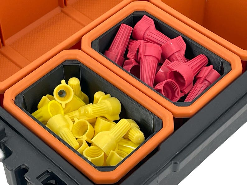 Op de afbeelding: Twee compartimenten van een oranje en zwarte gereedschapskist, elk gevuld met draadconnectoren. Het ene compartiment bevat rode draadconnectoren, het andere gele draadconnectoren.