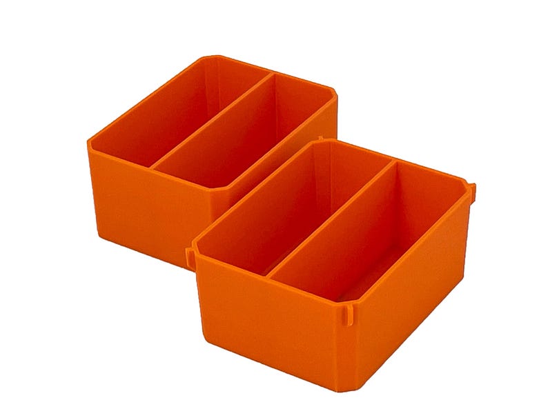 May include: Two orange plastic storage bins, each with three compartments. The rectangular bins have angled sides and a divider, creating three sections. The bins are empty and are set against a white background.