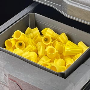 May include: A gray storage container filled with numerous yellow wire connectors. The connectors are various shapes and sizes, and are made of plastic. The container is inside a larger gray storage unit.