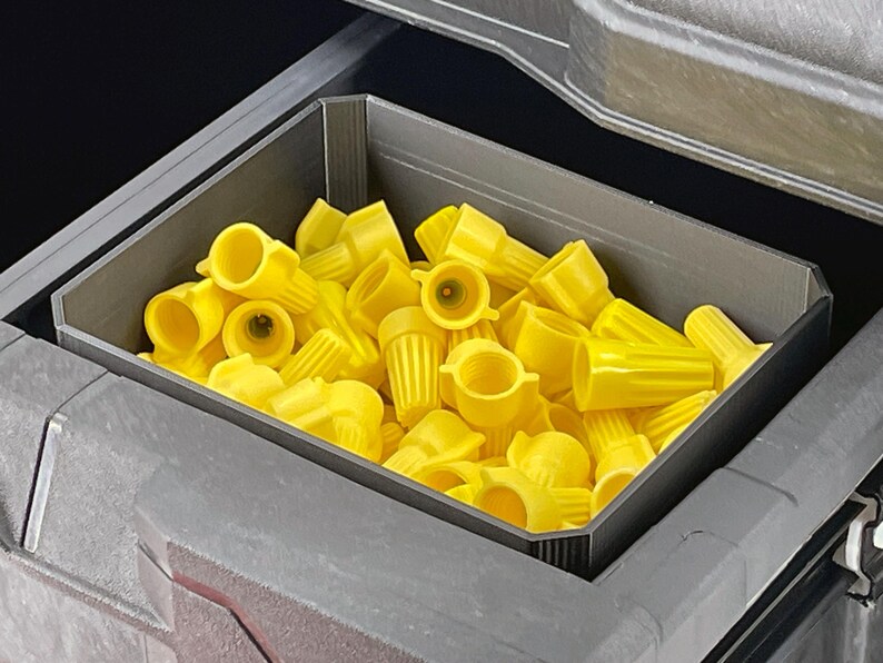 May include: A gray storage container filled with numerous yellow wire connectors. The connectors are various shapes and sizes, and are made of plastic. The container is inside a larger gray storage unit.
