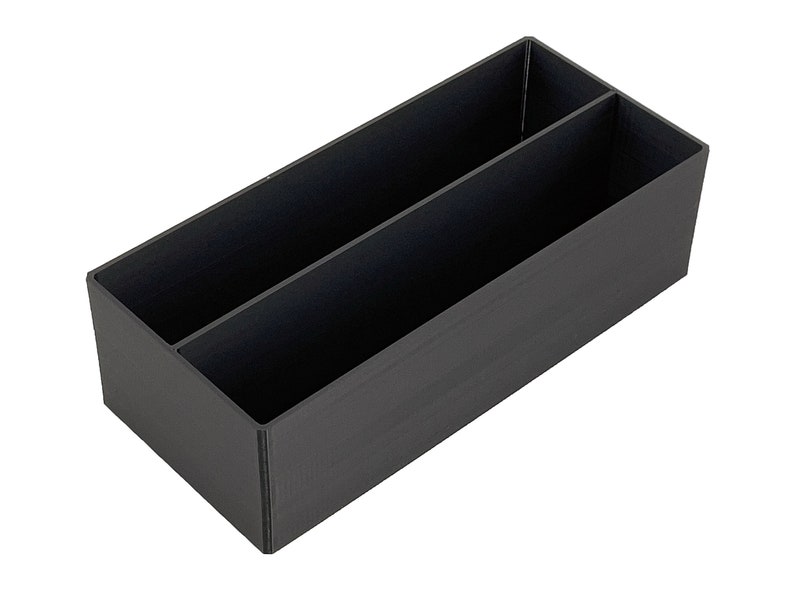 May include: A black plastic storage box with two compartments. The box is rectangular and has a smooth surface.