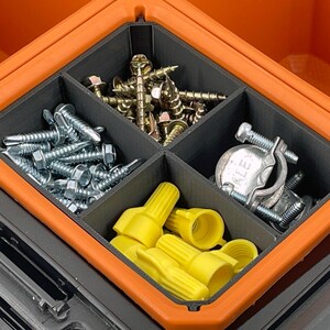 Op de afbeelding: Een oranje en zwarte gereedschapskist met een verdeeld interieur, gevuld met diverse hardware-artikelen. De compartimenten bevatten zilveren schroeven, gouden schroeven, gele draadverbinders en metalen klemmen.