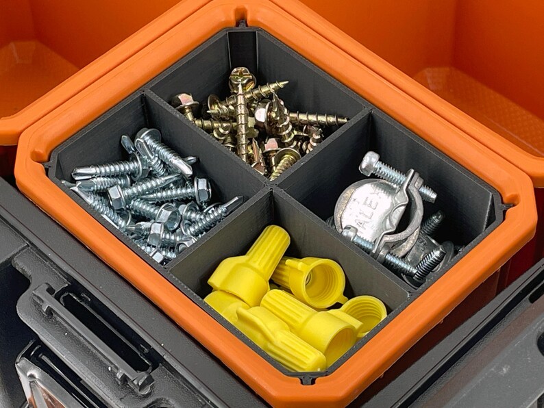 Op de afbeelding: Een oranje en zwarte gereedschapskist met een verdeeld interieur, gevuld met diverse hardware-artikelen. De compartimenten bevatten zilveren schroeven, gouden schroeven, gele draadverbinders en metalen klemmen.
