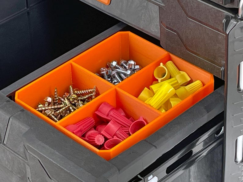 May include: An open drawer with an orange organizer containing various hardware items. The compartments hold screws, bolts, wire connectors, and other small parts. The drawer is part of a larger black storage system.