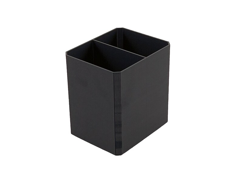May include: A black desk organizer with two compartments. The organizer is a rectangular prism shape with a vertical divider. The exterior is a matte black finish. The organizer is designed to hold pens, pencils, and other office supplies.