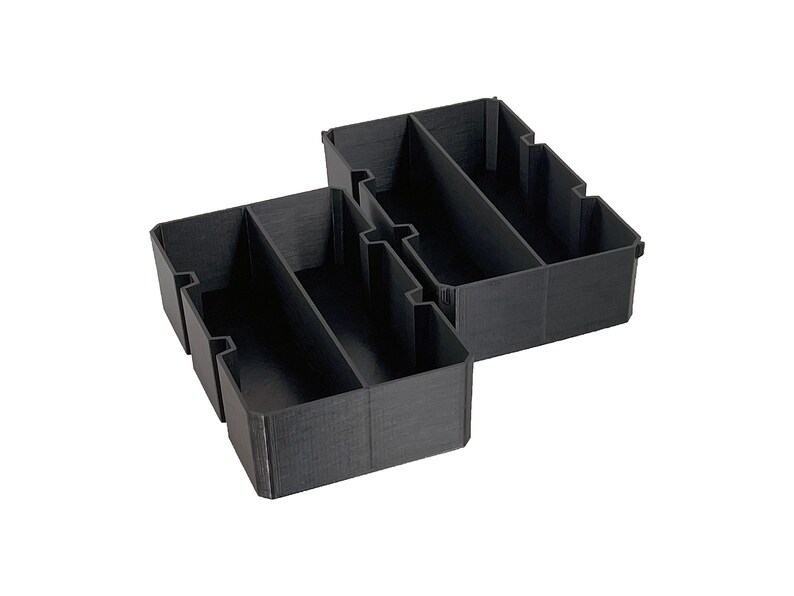 May include: Two black, rectangular storage organizers with multiple compartments. The organizers are made of a textured material and are designed to fit inside a drawer or cabinet. The compartments are divided by vertical dividers.