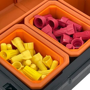 Puede incluir: Una caja de almacenamiento de pl&aacute;stico negro con dos compartimentos naranjas llenos de conectores de alambre rojos y amarillos.